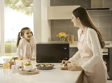 Due persone in cucina moderna con microonde LG: una donna e una bambina preparano il cibo su un tavolo.