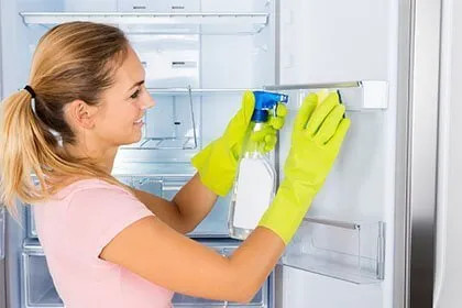 Donna con guanti gialli pulisce l’interno di un frigorifero LG bianco, rimuovendo residui con un panno.