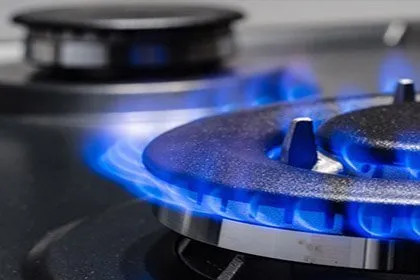 Bruciatore a gas acceso con fiamma blu su piano cottura LG, primo piano di una griglia metallica.