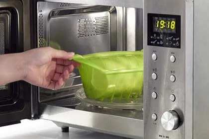 Mano inserisce un contenitore verde nel microonde LG, display digitale mostra l’ora 19:18.